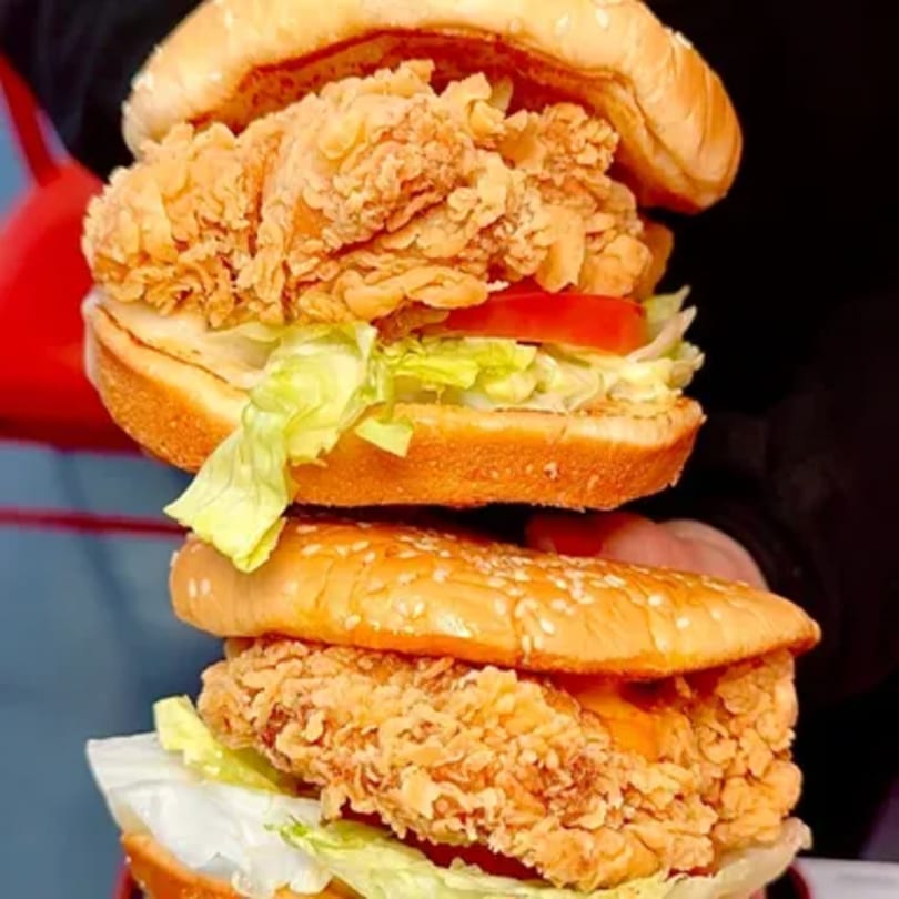 Two stacked Cluck & Crispy chicken sandwiches with lettuce, tomato, and sesame seed buns.