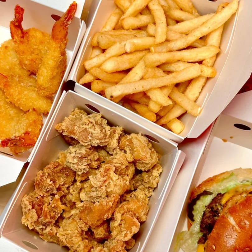 Fried shrimp, crispy chicken pieces, golden french fries, and a cheeseburger in takeout boxes.