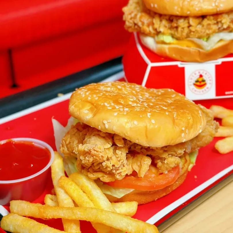 Crispy chicken sandwich with lettuce, tomato, fries, and ketchup on a red tray.